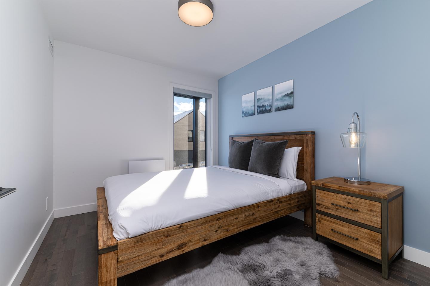 Chambre moderne avec lit en bois, mur bleu, et lampes.