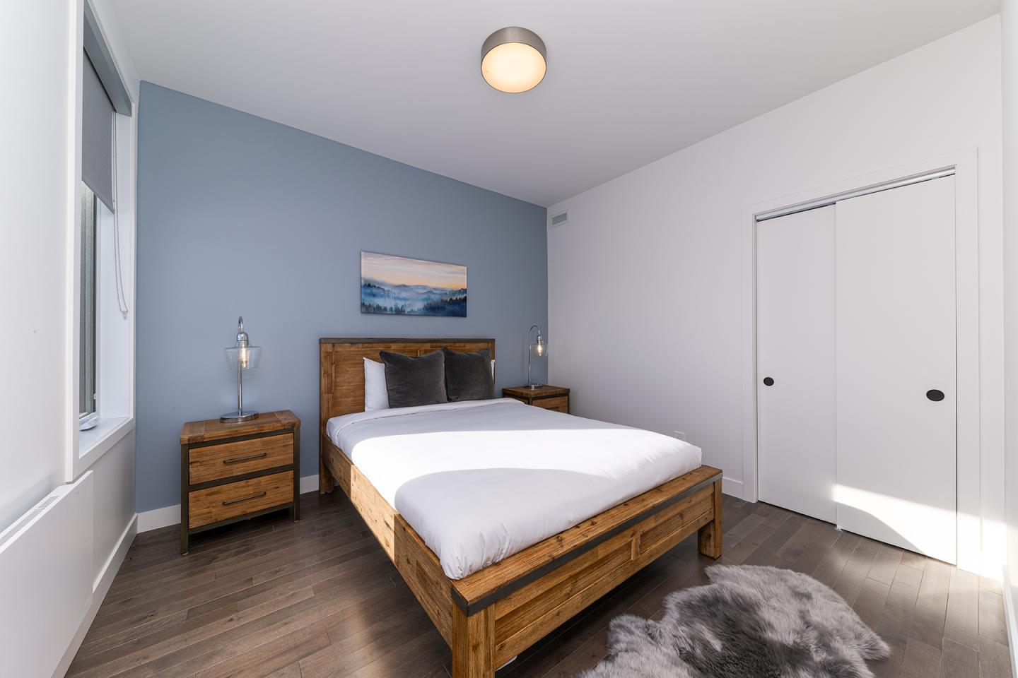 Chambre moderne avec lit double, murs bleu et blanc, et lampe sur table de chevet.