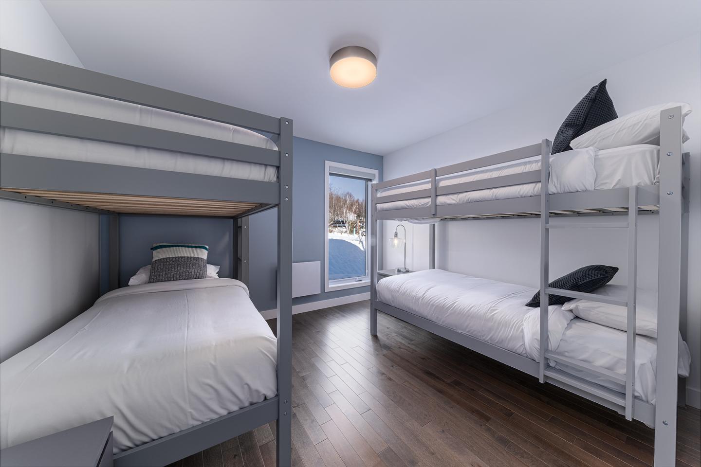 Chambre avec lits superposés et fenêtre, sol en bois, murs clairs.
