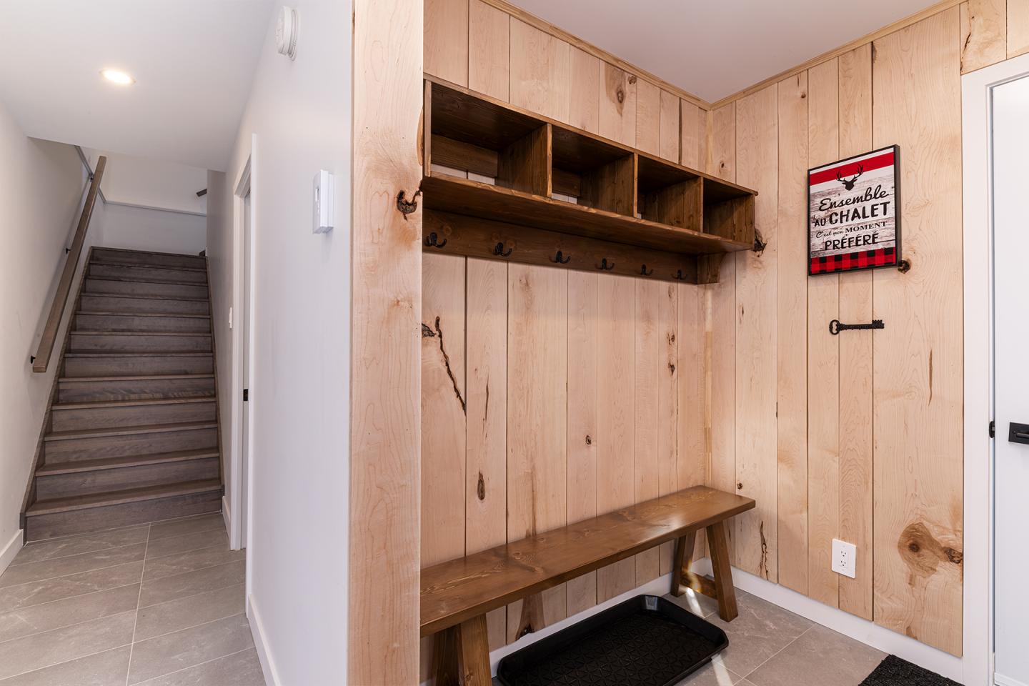 Entrée avec banc en bois, étagères, mur en bois clair. Escalier à gauche.