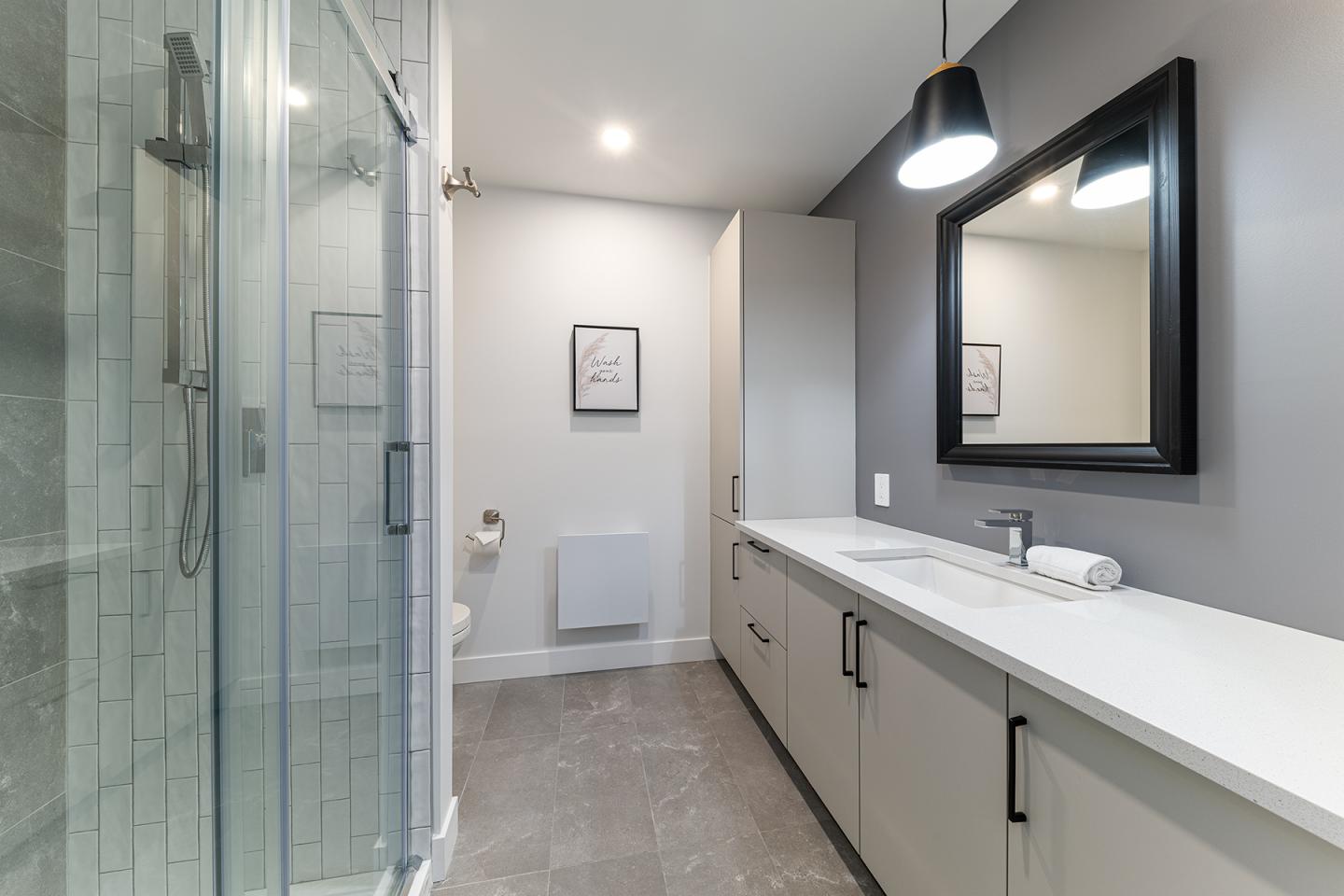 Salle de bain moderne avec douche vitrée, miroir noir et lavabo blanc.