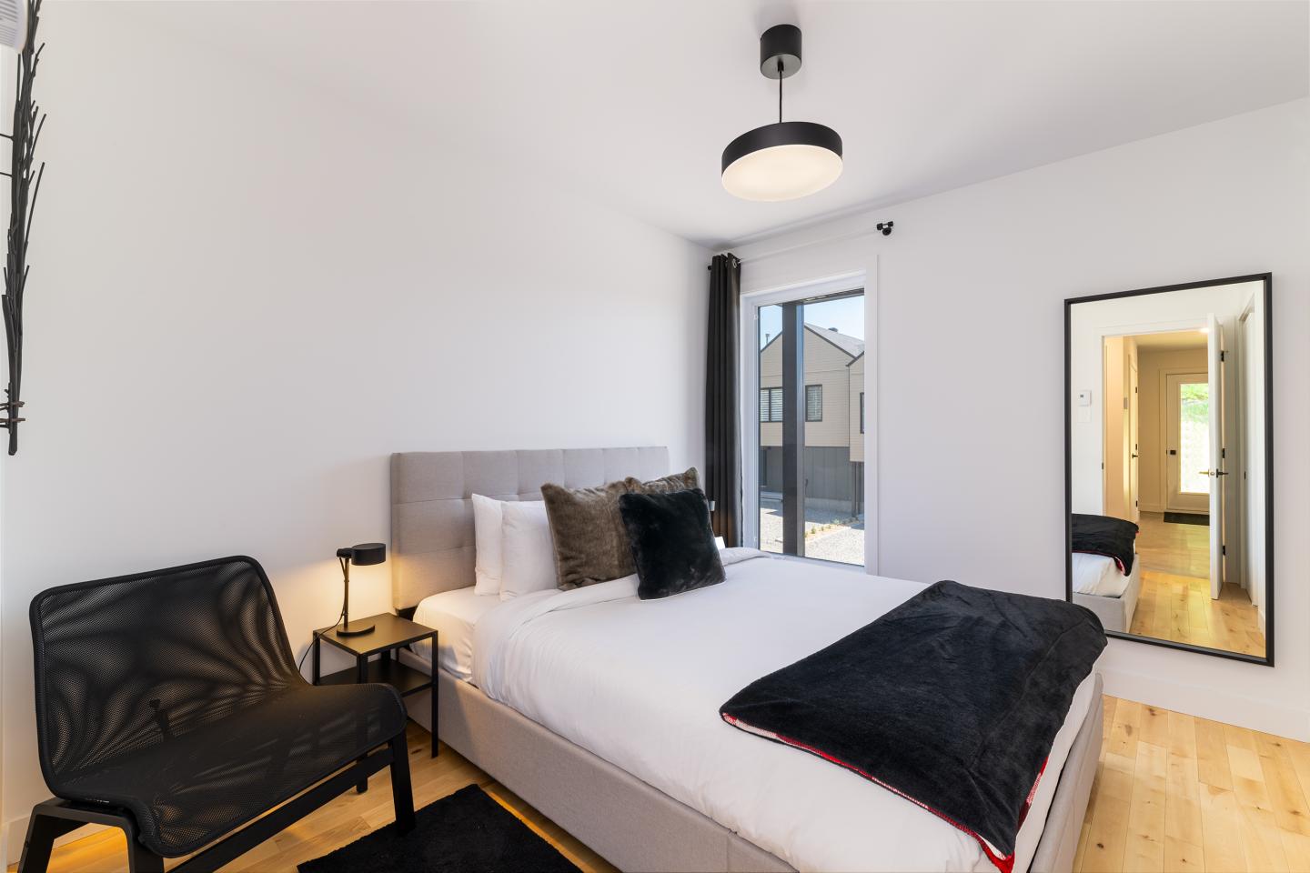 Chambre moderne avec lit double, miroir et chaise noire.