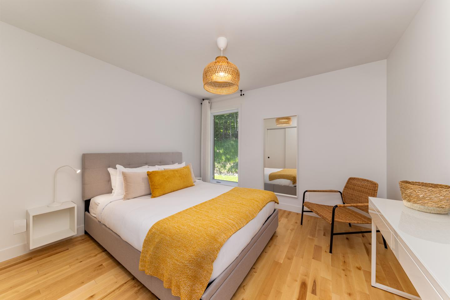 Chambre moderne avec lit double, couverture jaune, et chaise en osier.
