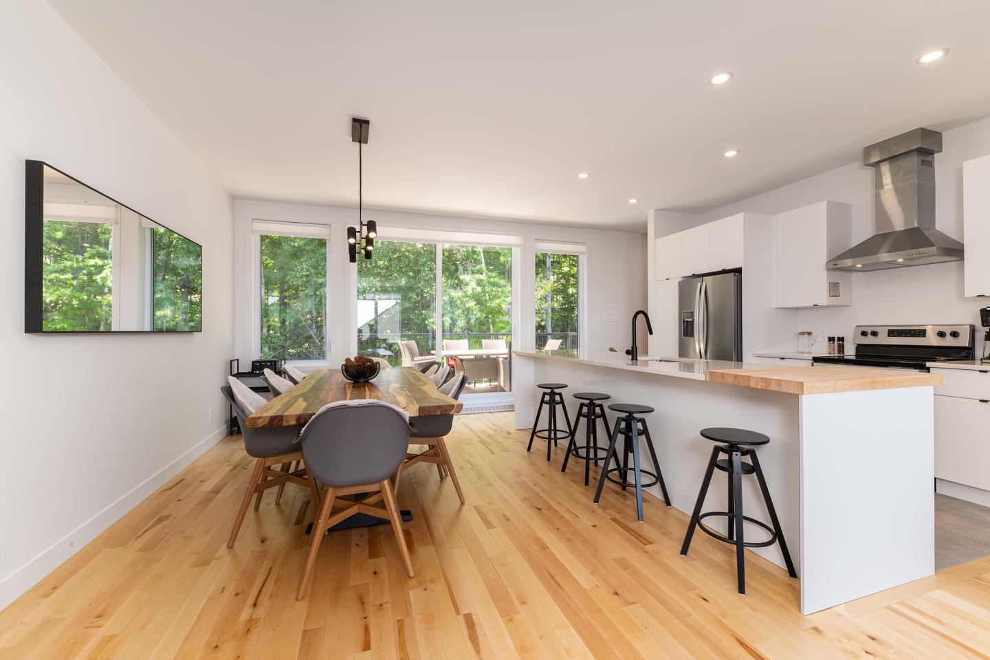 Salle à manger moderne avec table en bois, chaises grises et cuisine ouverte.