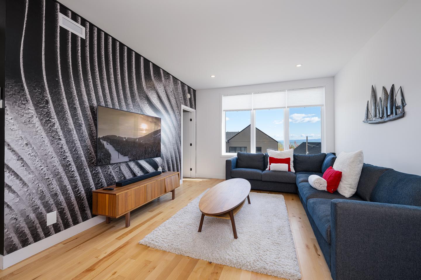 Salon moderne avec canapé bleu, mur graphique noir et blanc, et grande fenêtre.
