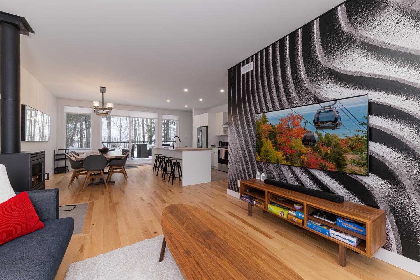 Salon moderne avec un mur décoratif noir et blanc, TV, canapé gris, table en bois.