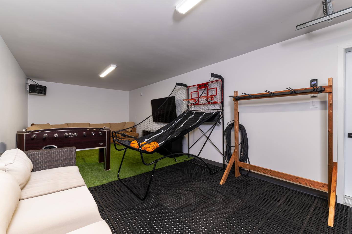 Salle de jeux avec baby-foot, panier de basket, et canapé beige.