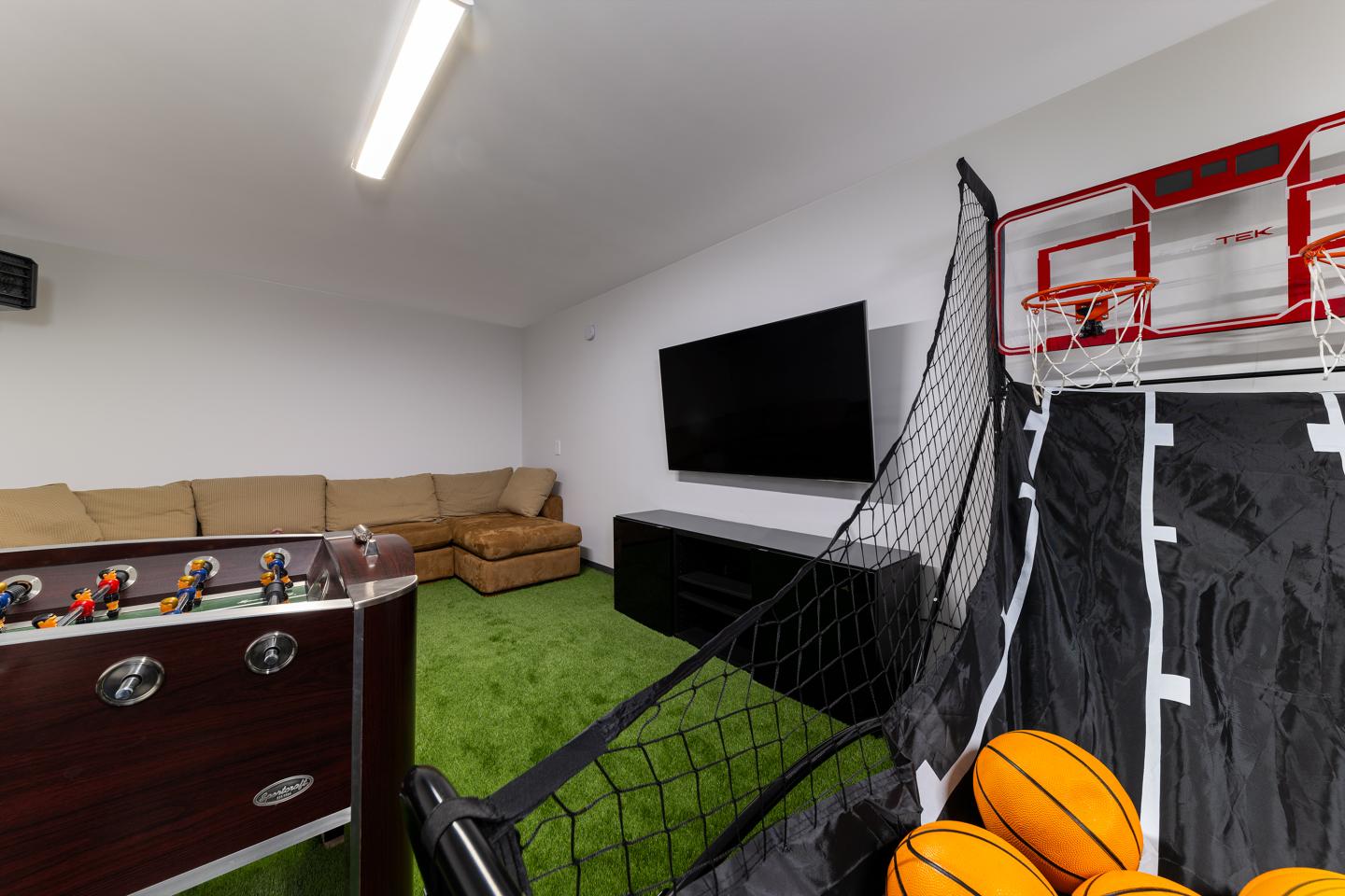 Salle de jeux avec canapé, babyfoot, panier de basket et TV.