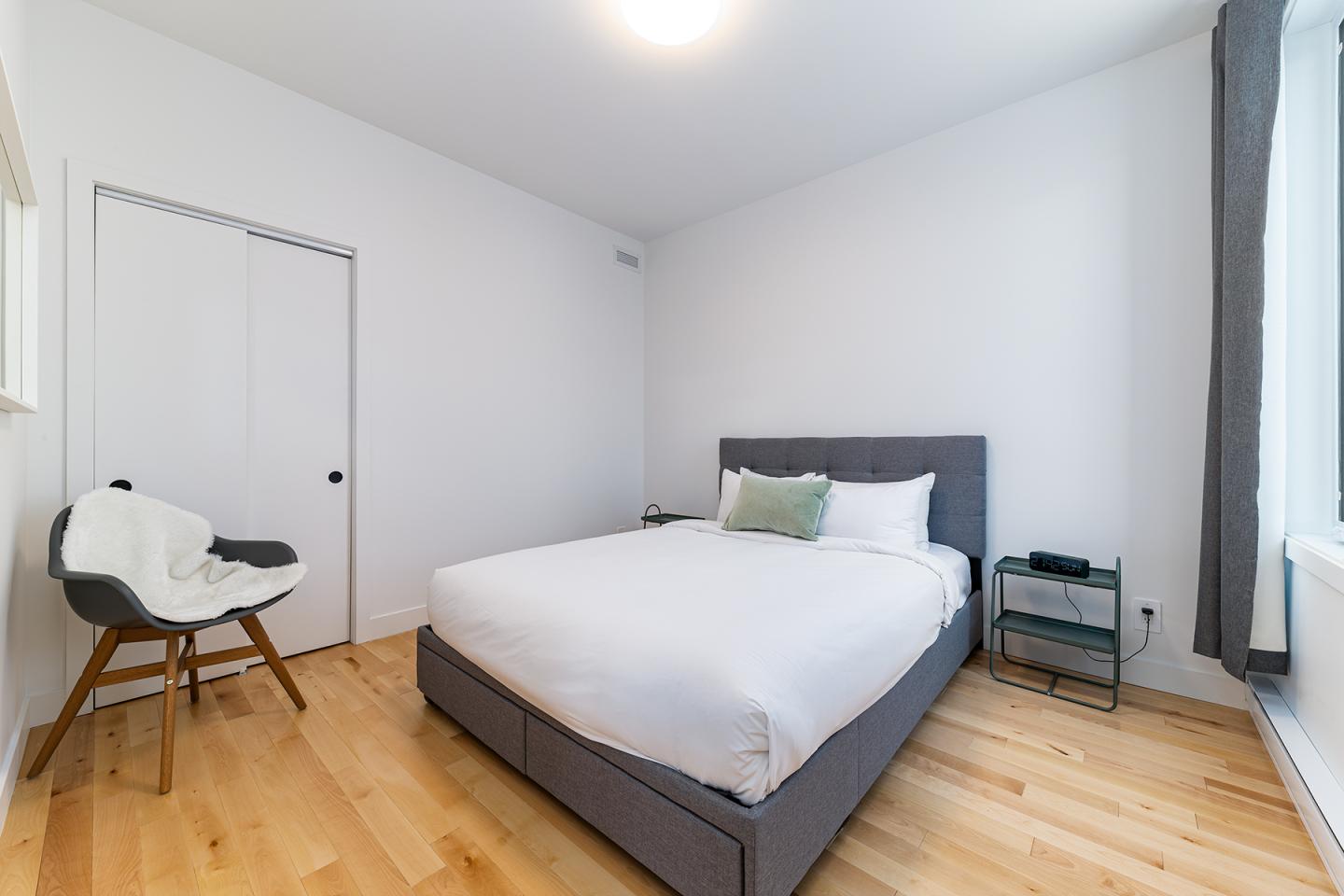 Chambre moderne, lit double, parquet clair, chaises, murs blancs.