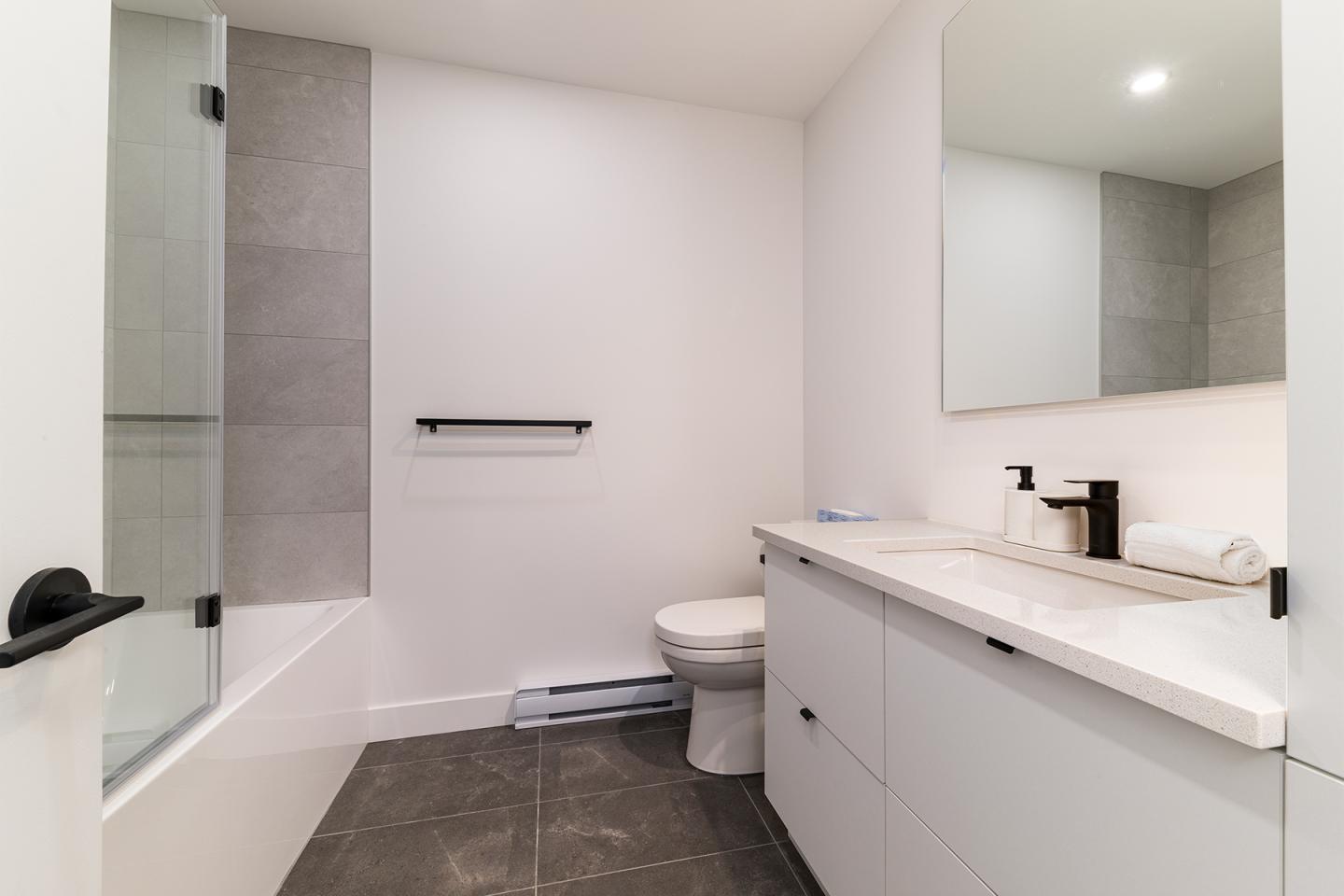 Salle de bain moderne avec baignoire, lavabo et carreaux gris.