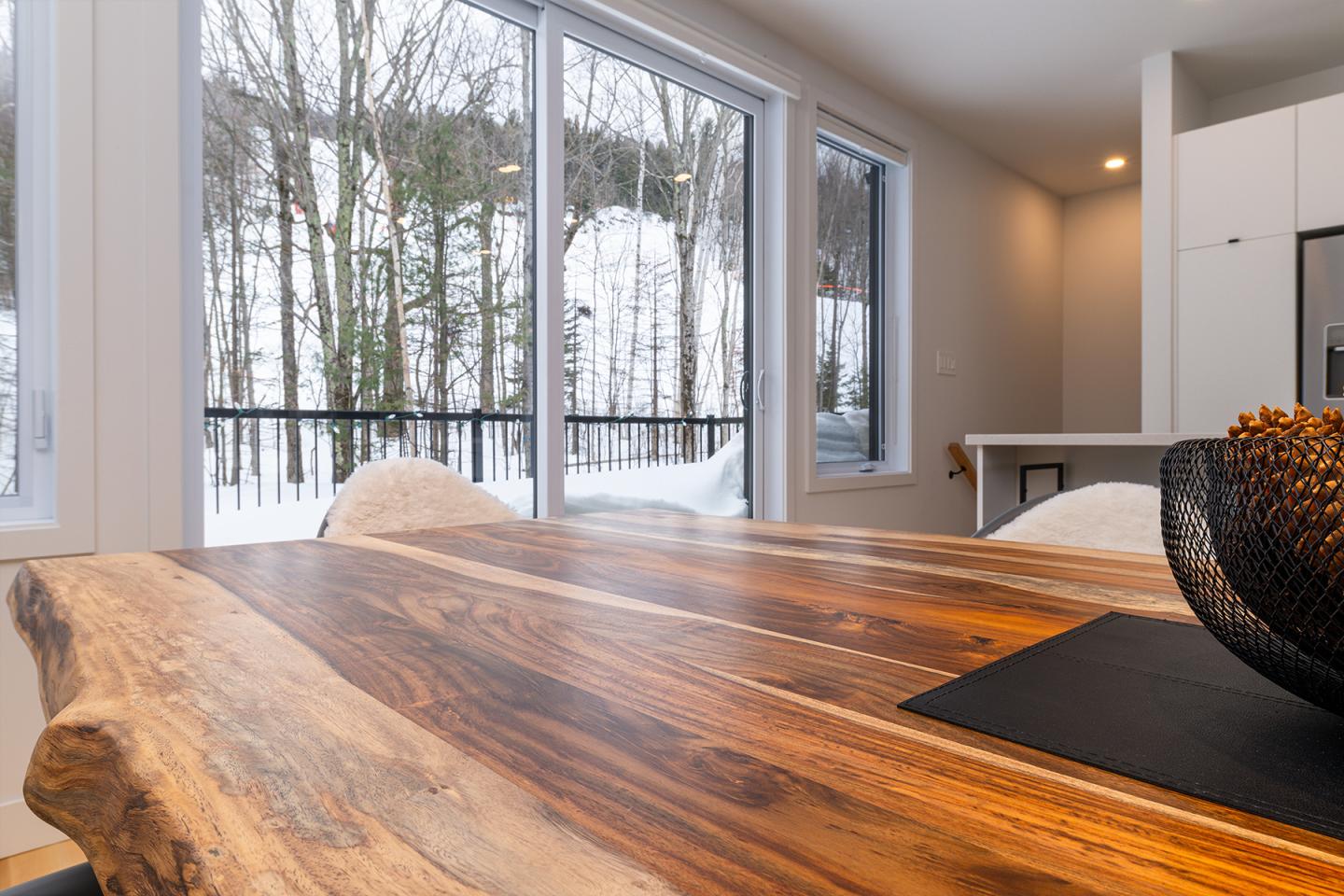 Table en bois près de fenêtres avec vue sur forêt enneigée.