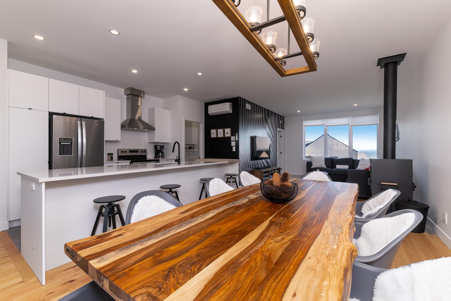 Cuisine moderne avec table en bois, luminaires suspendus et grandes fenêtres.