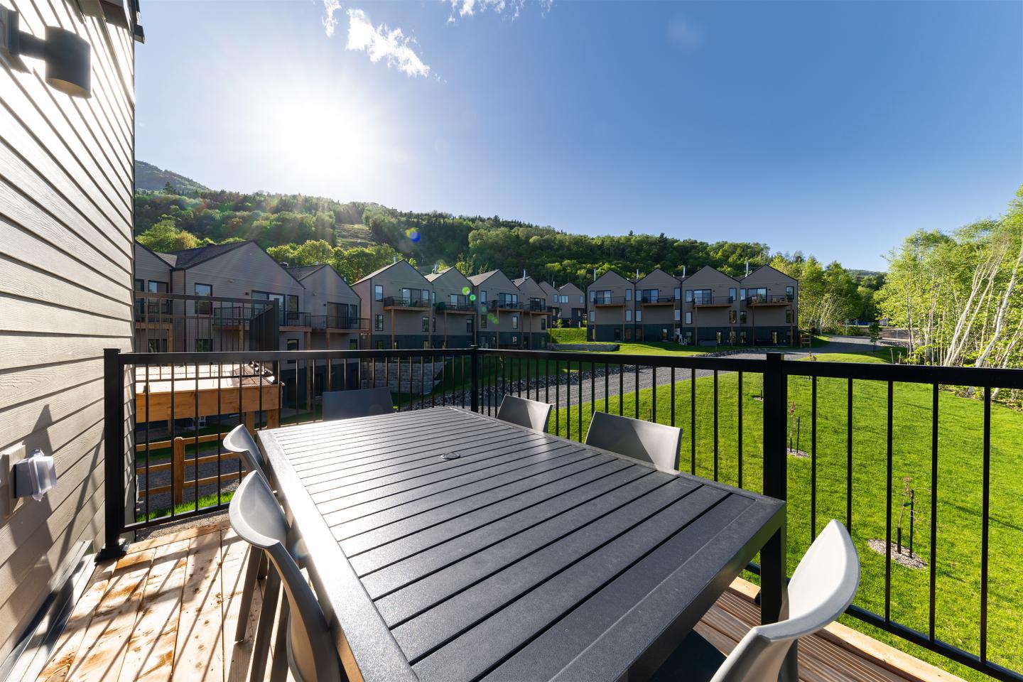 Terrasse ensoleillée, table et chaises, vue sur pelouse et collines.