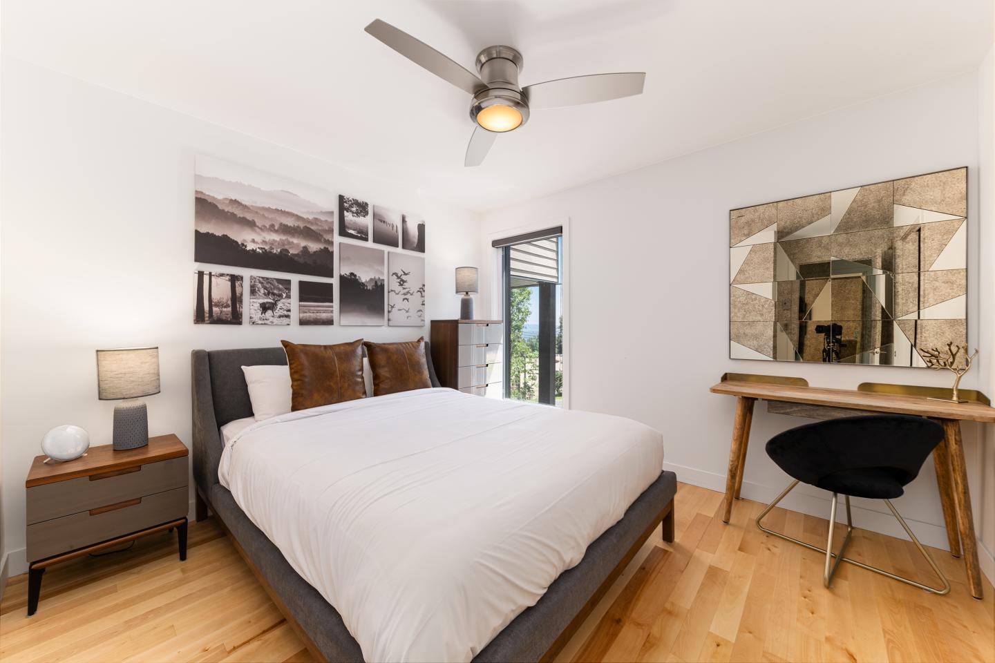 Chambre moderne avec lit, ventilateur au plafond, bureau et miroir sur mur blanc.