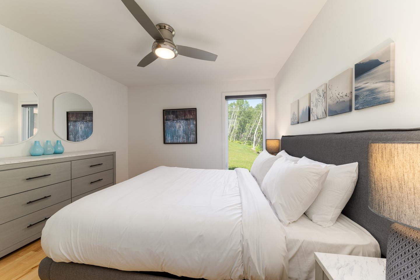 Chambre lumineuse avec lit double, ventilateur au plafond et tableaux muraux.