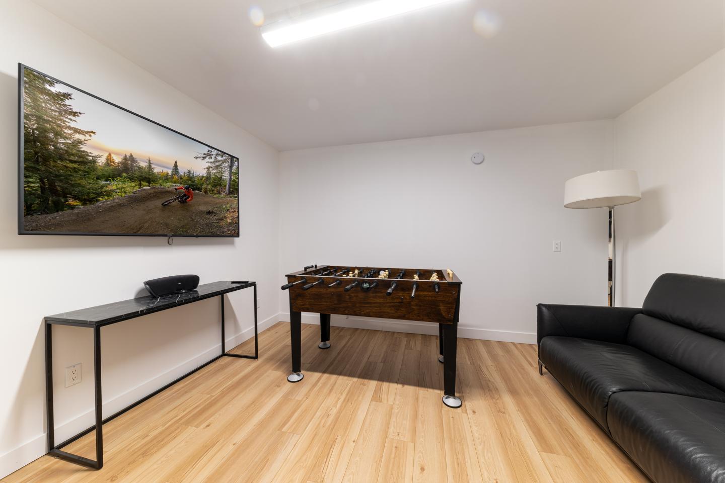 Salle avec canapé noir, baby-foot et télévision murale.