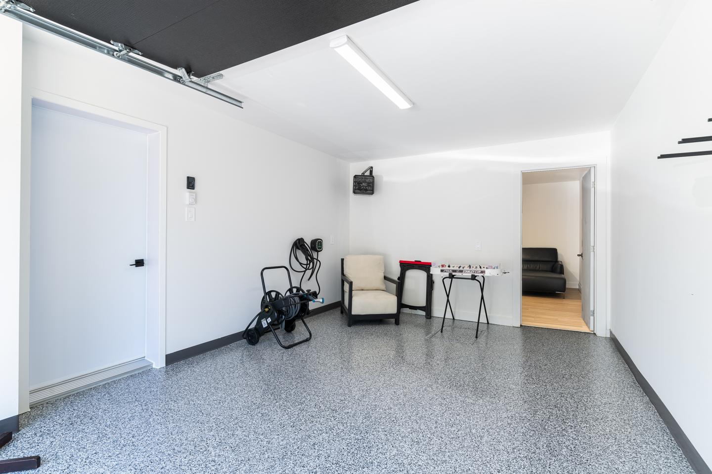 Salle blanche avec chaise, vélo pliant, table et fauteuil noir au fond.