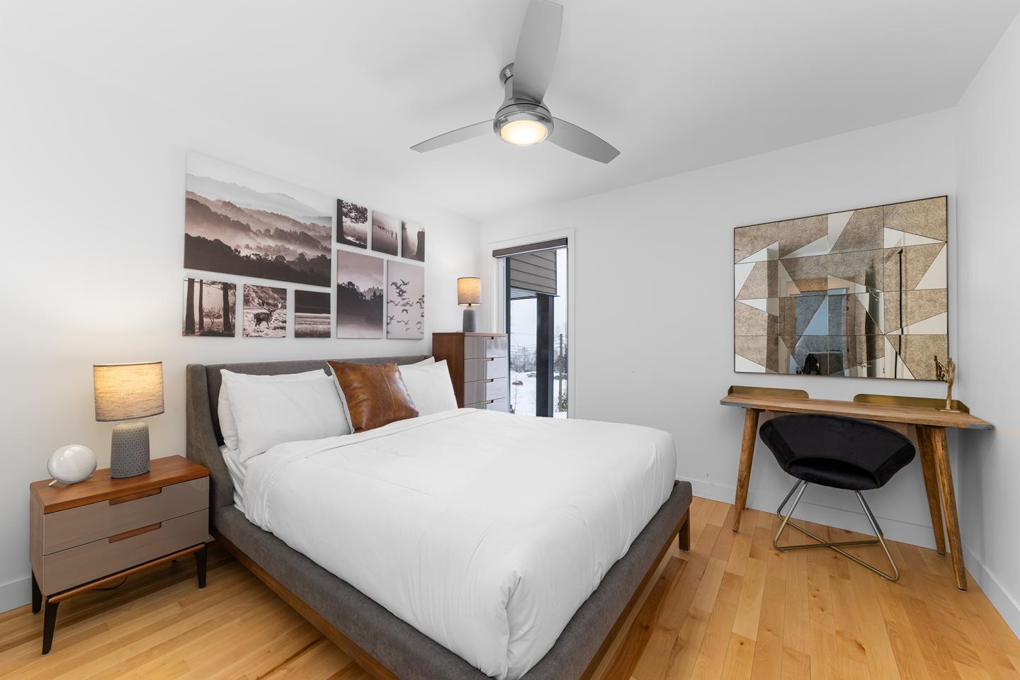 Chambre minimaliste avec lit, ventilateur, bureau et tableau photos.