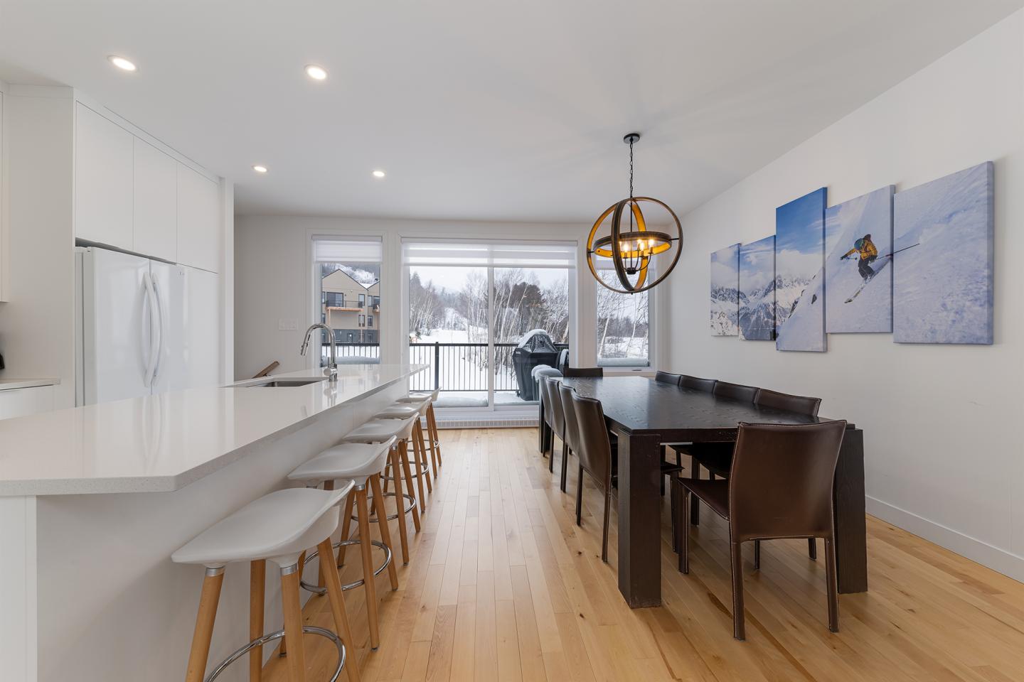 Cuisine moderne avec îlot, table à manger, et vues sur neige. Lustre sphérique suspendu.