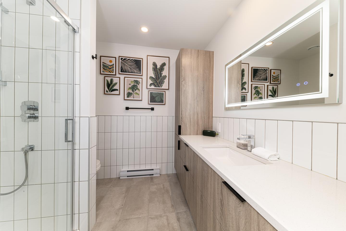 Salle de bain moderne avec douche vitrée, lavabo et mur de cadres.