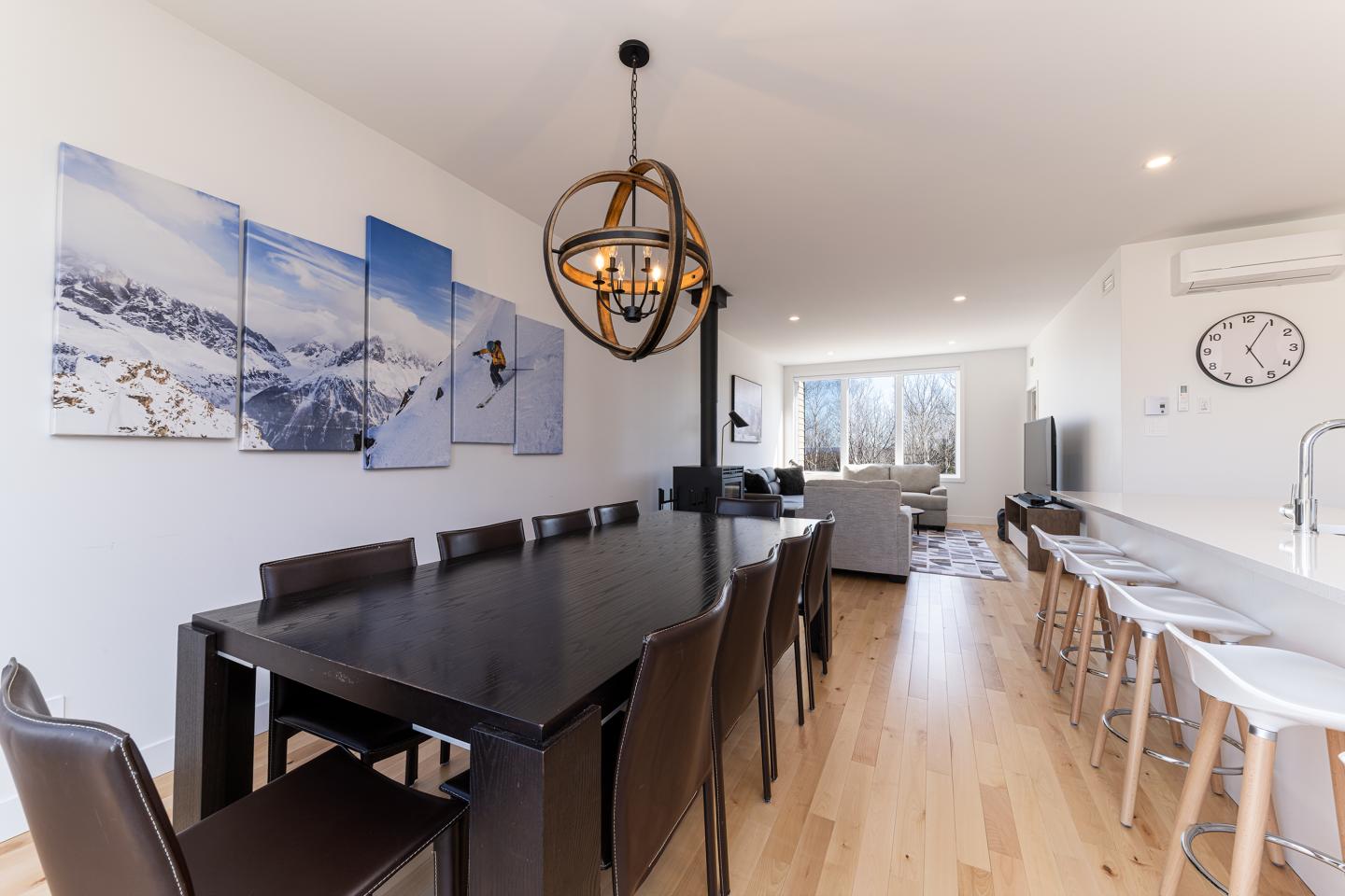 Salle à manger moderne avec table en bois sombre et chaises en cuir, cuisine ouverte.