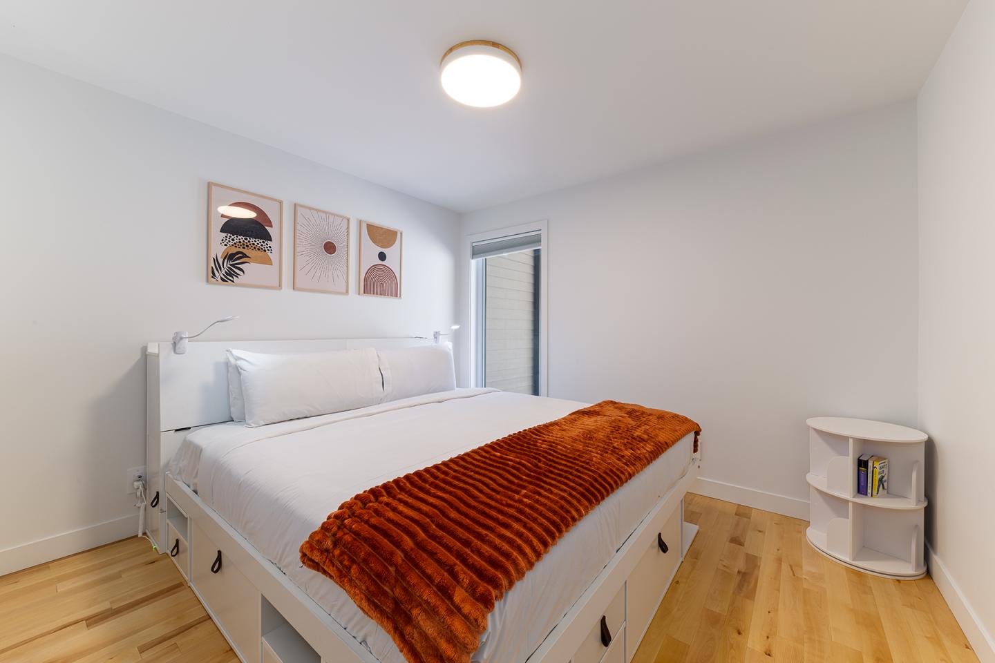 Chambre lumineuse avec lit blanc, couvre-lit orange, murs minimalistes.