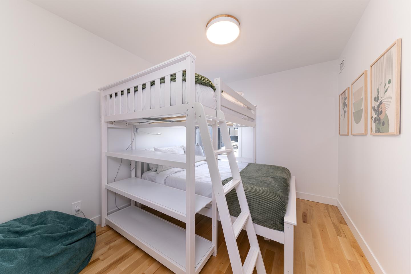Lit superposé blanc dans une chambre lumineuse avec parquet et cadres muraux.