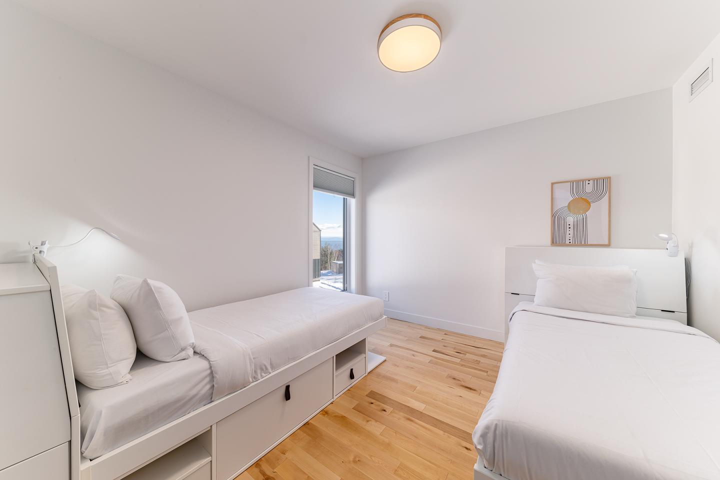 Deux lits simples dans une chambre blanche, parquet en bois clair, tableau au mur.