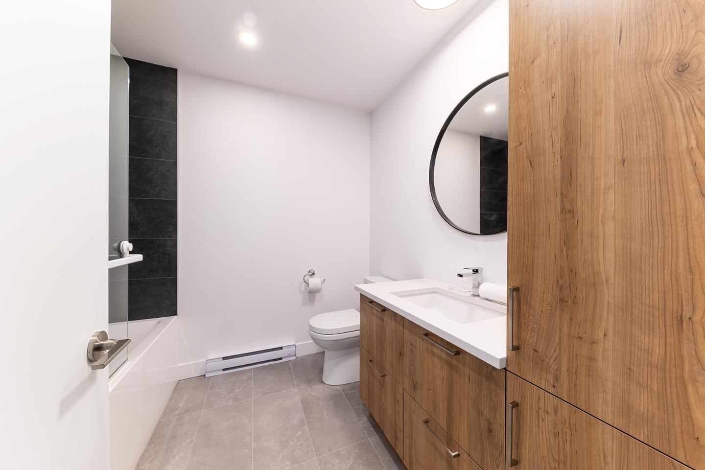 Salle de bain moderne, bois clair, lavabo rond, baignoire, toilettes.