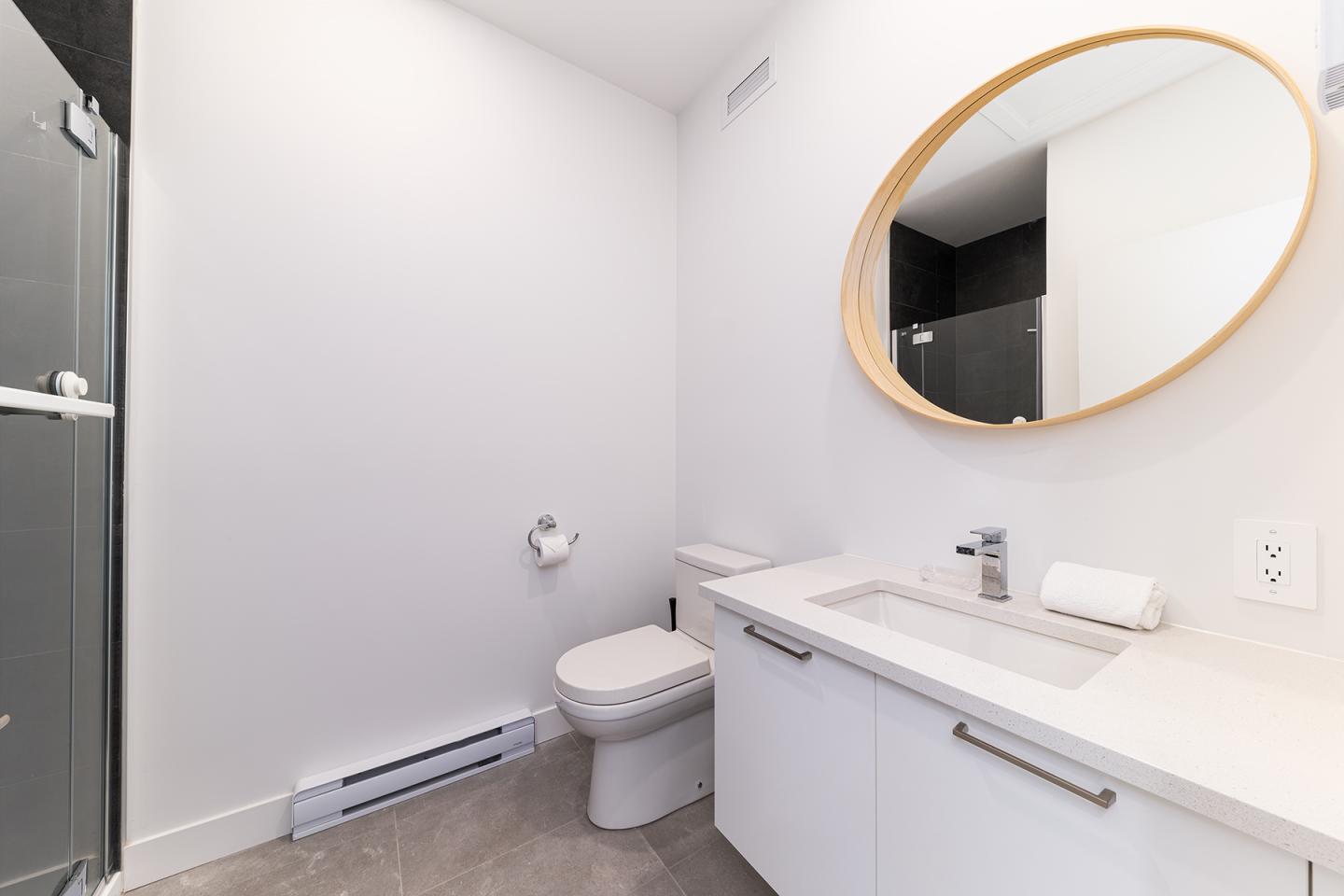 Salle de bain moderne avec lavabo, toilette et miroir ovale.