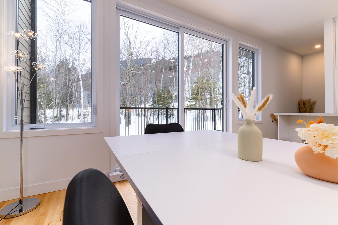 Salle à manger moderne avec vue enneigée, table blanche et vases décoratifs.
