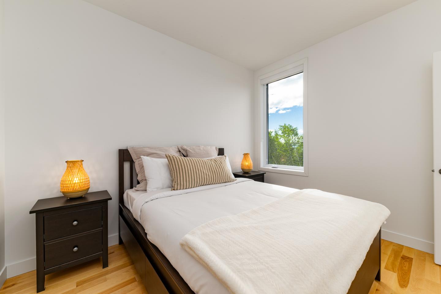 Chambre lumineuse avec lit double, table de chevet et vue sur jardin par la fenêtre.
