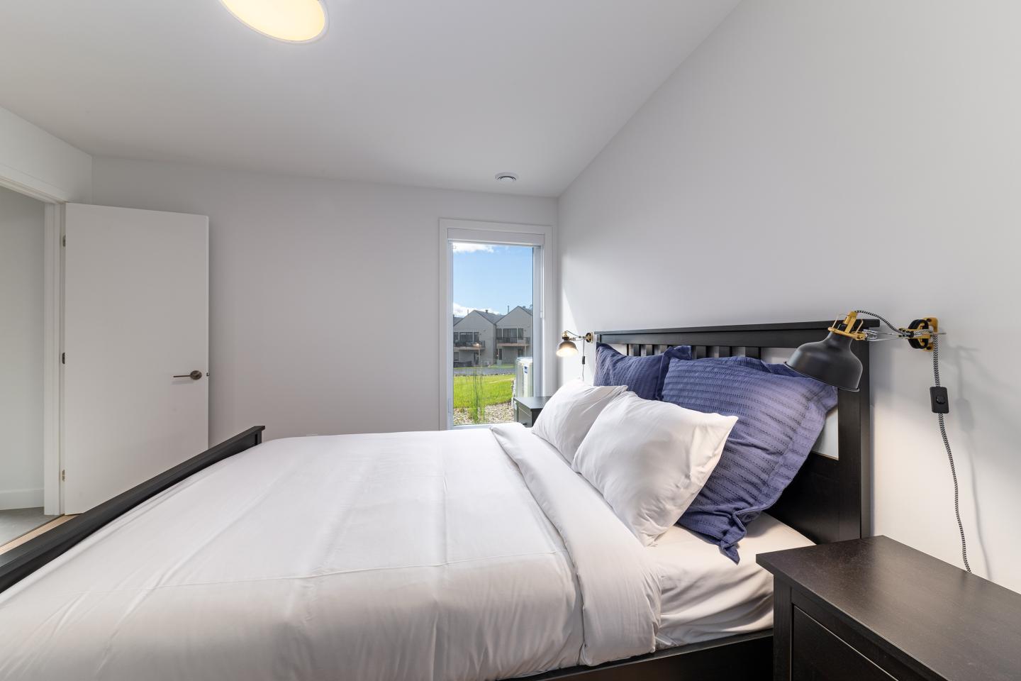 Chambre moderne avec lit fait, grandes fenêtres, murs blancs.