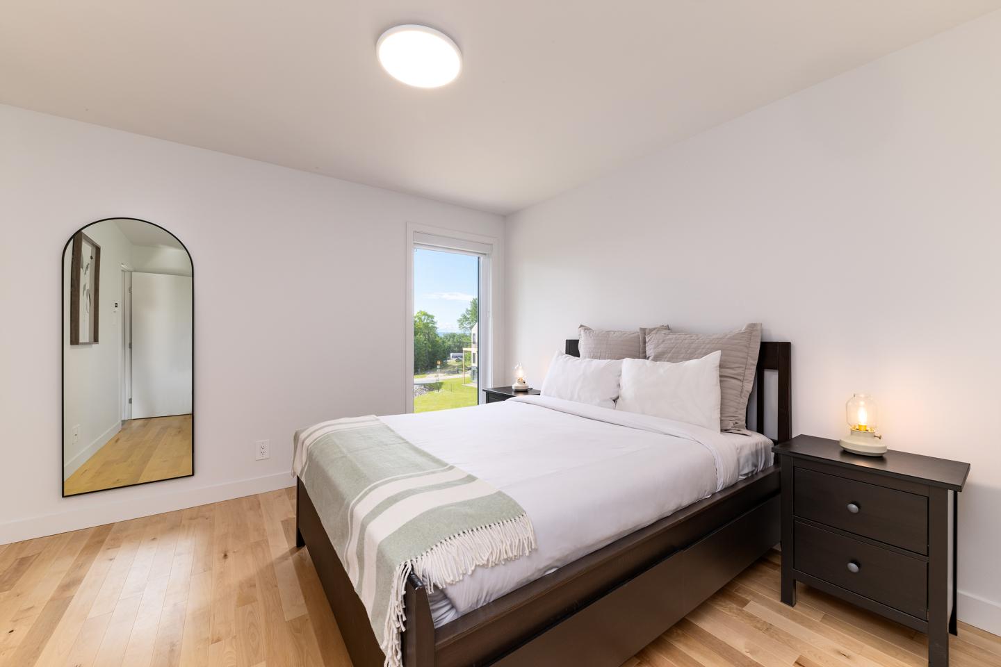 Chambre minimaliste avec lit double, miroir et lumière naturelle.