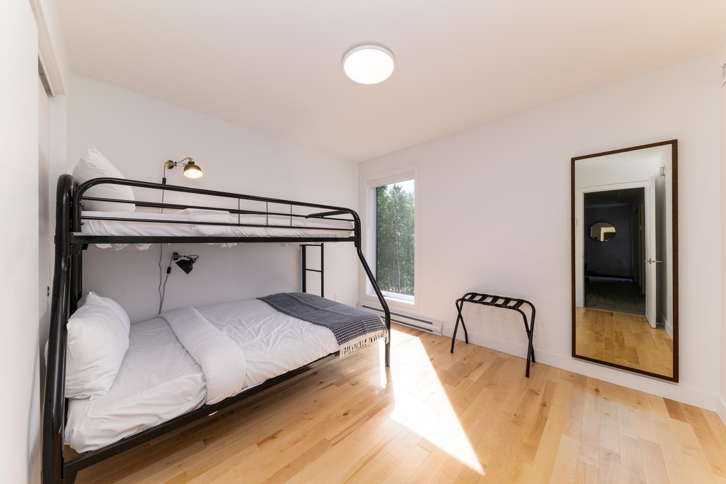 Chambre avec lits superposés, miroir et parquet en bois clair.