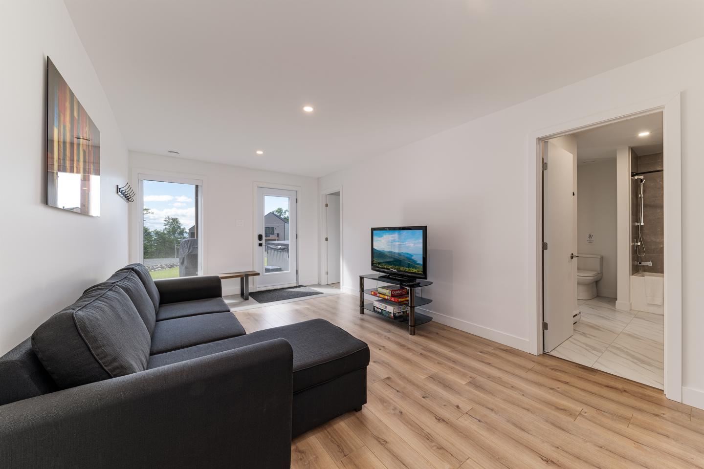 Salon moderne avec un canapé sombre, téléviseur et parquet clair.