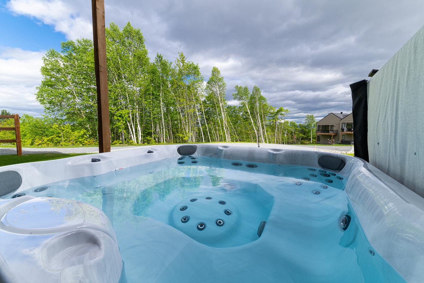 Jacuzzi extérieur avec vue sur des arbres et ciel nuageux.