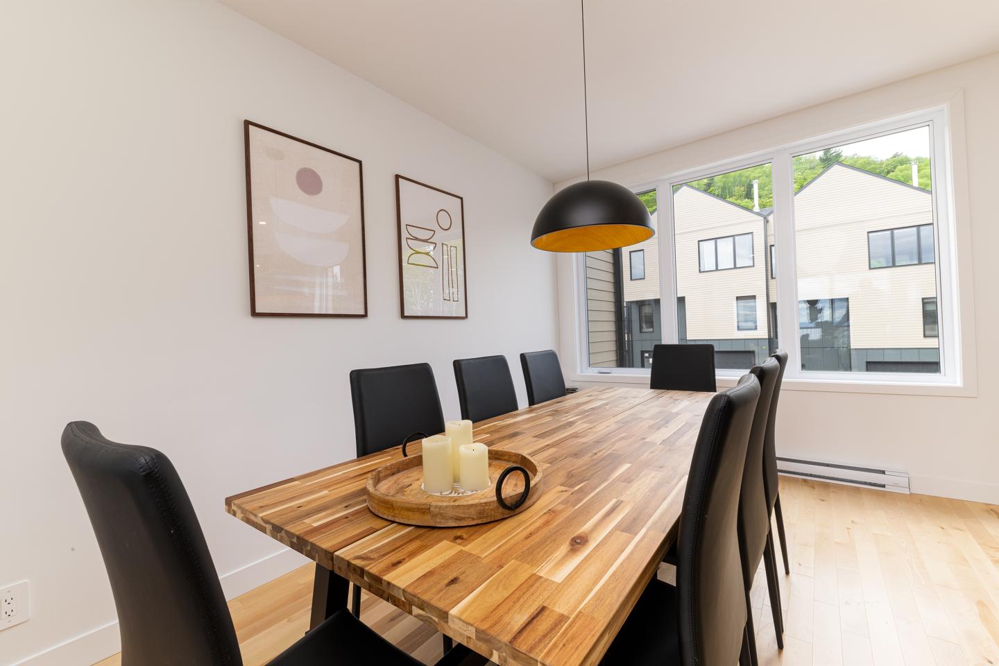 Salle à manger moderne avec table en bois, chaises noires et grande fenêtre.
