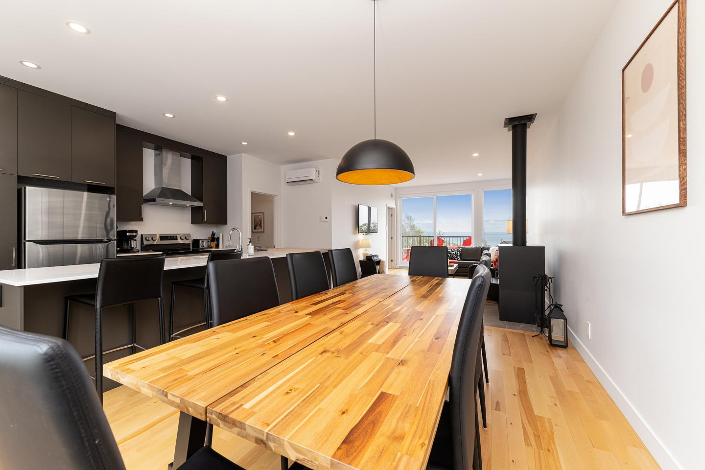 Salle à manger moderne avec table en bois, chaises noires et lumière naturelle.