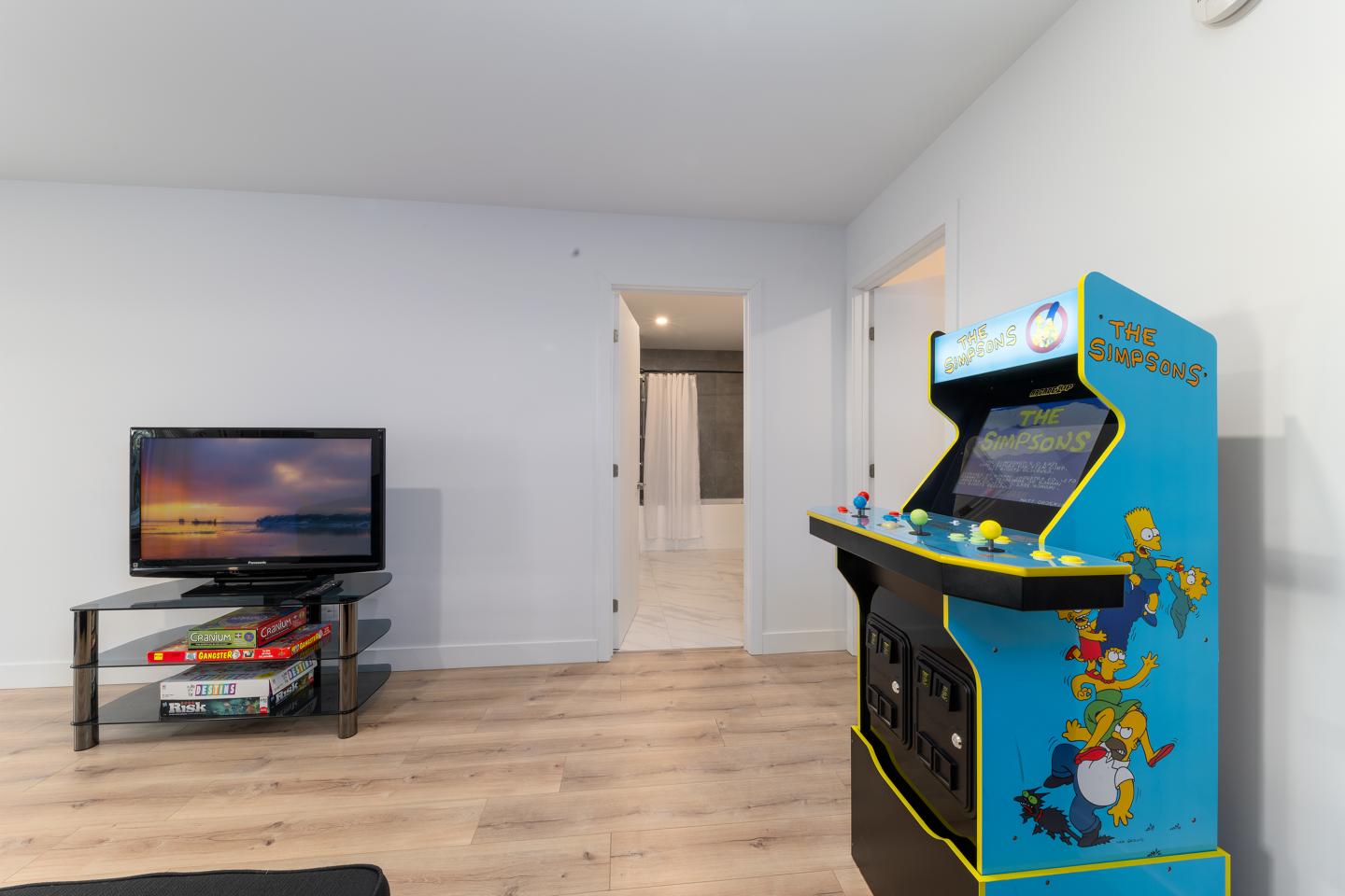 Salle de jeux avec borne d'arcade bleue et télé sur un meuble noir.