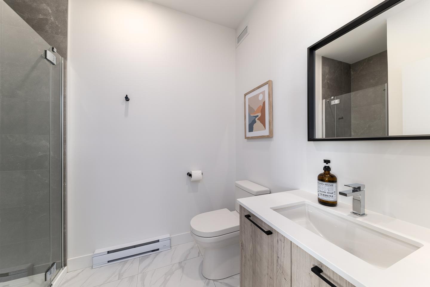 Salle de bains moderne, murs blancs, douche vitrée, lavabo avec miroir.