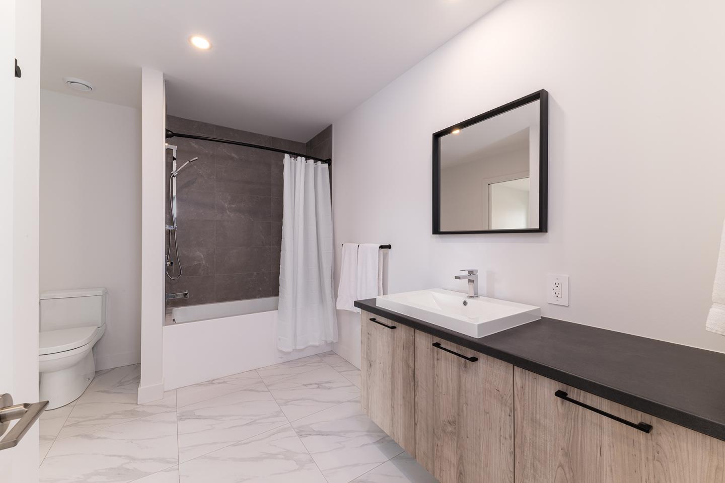Salle de bain moderne avec carrelage blanc, lavabo sur meuble en bois, baignoire et miroir.