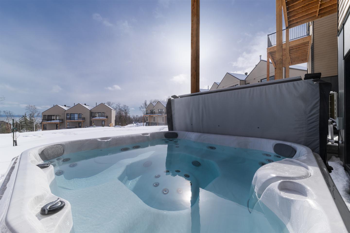 Jacuzzi extérieur en hiver, ciel bleu, maisons au fond.