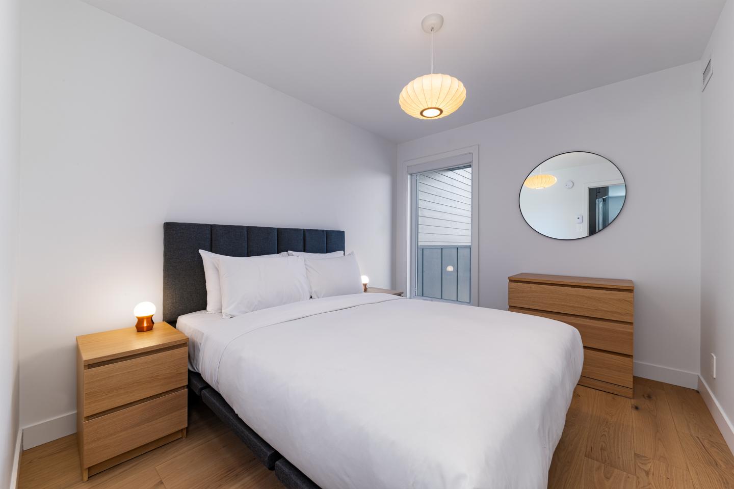 Chambre moderne avec lit blanc, miroirs et meubles en bois.