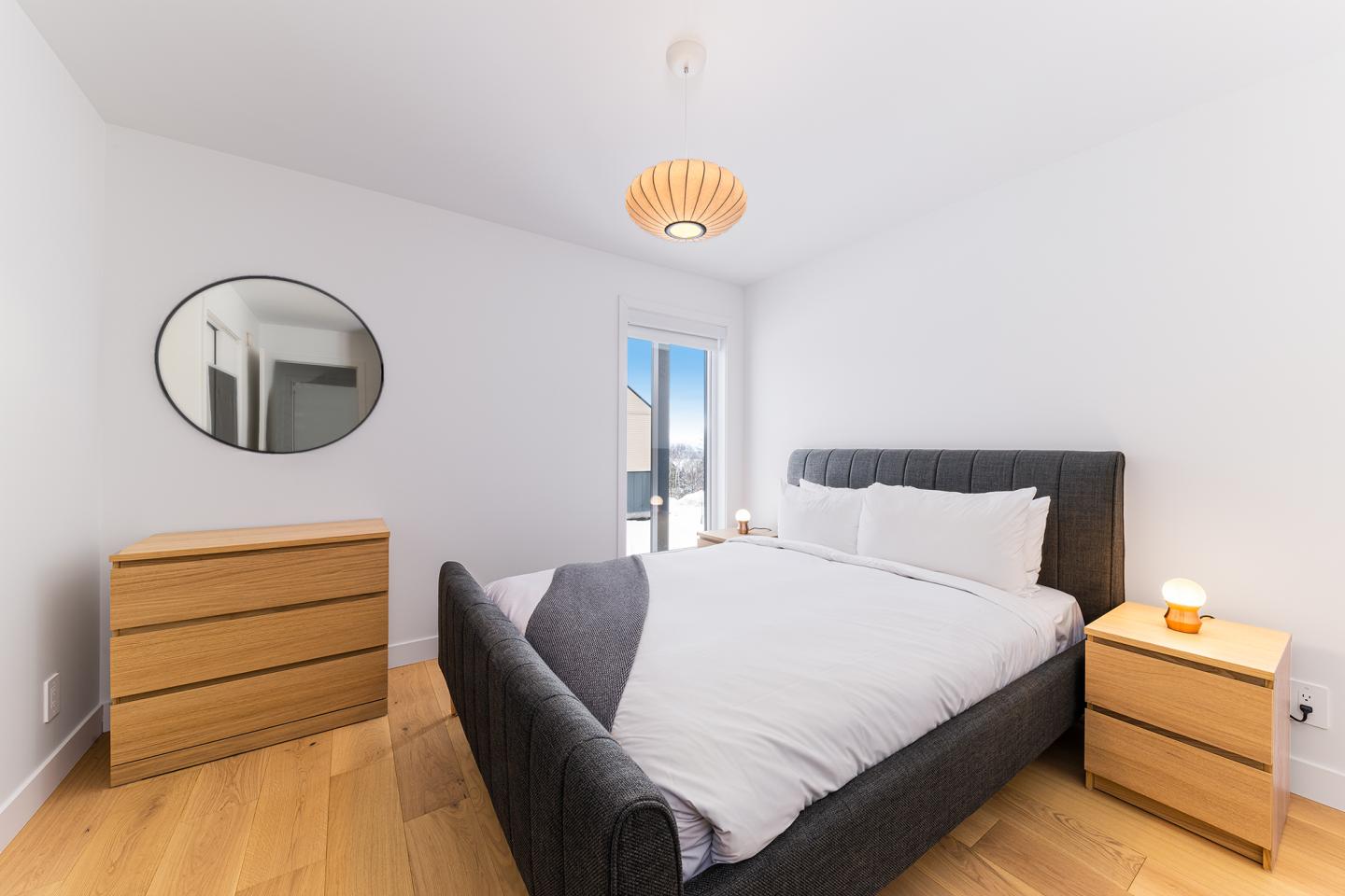 Chambre lumineuse avec lit double, commode en bois et miroir rond.