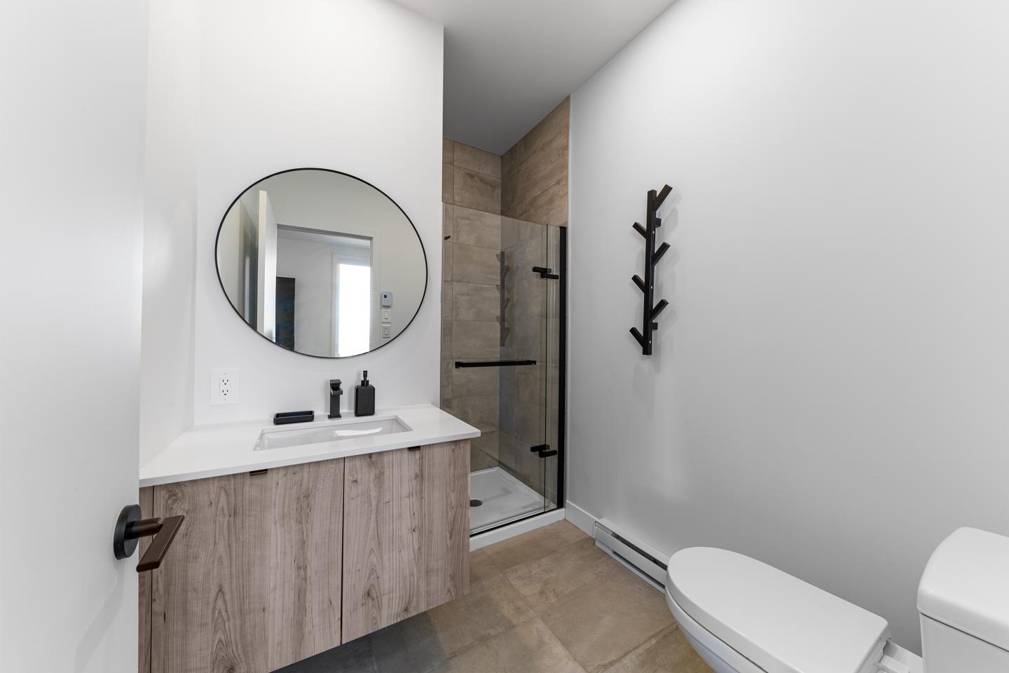 Salle de bain moderne avec douche, miroir rond et lavabo en bois.