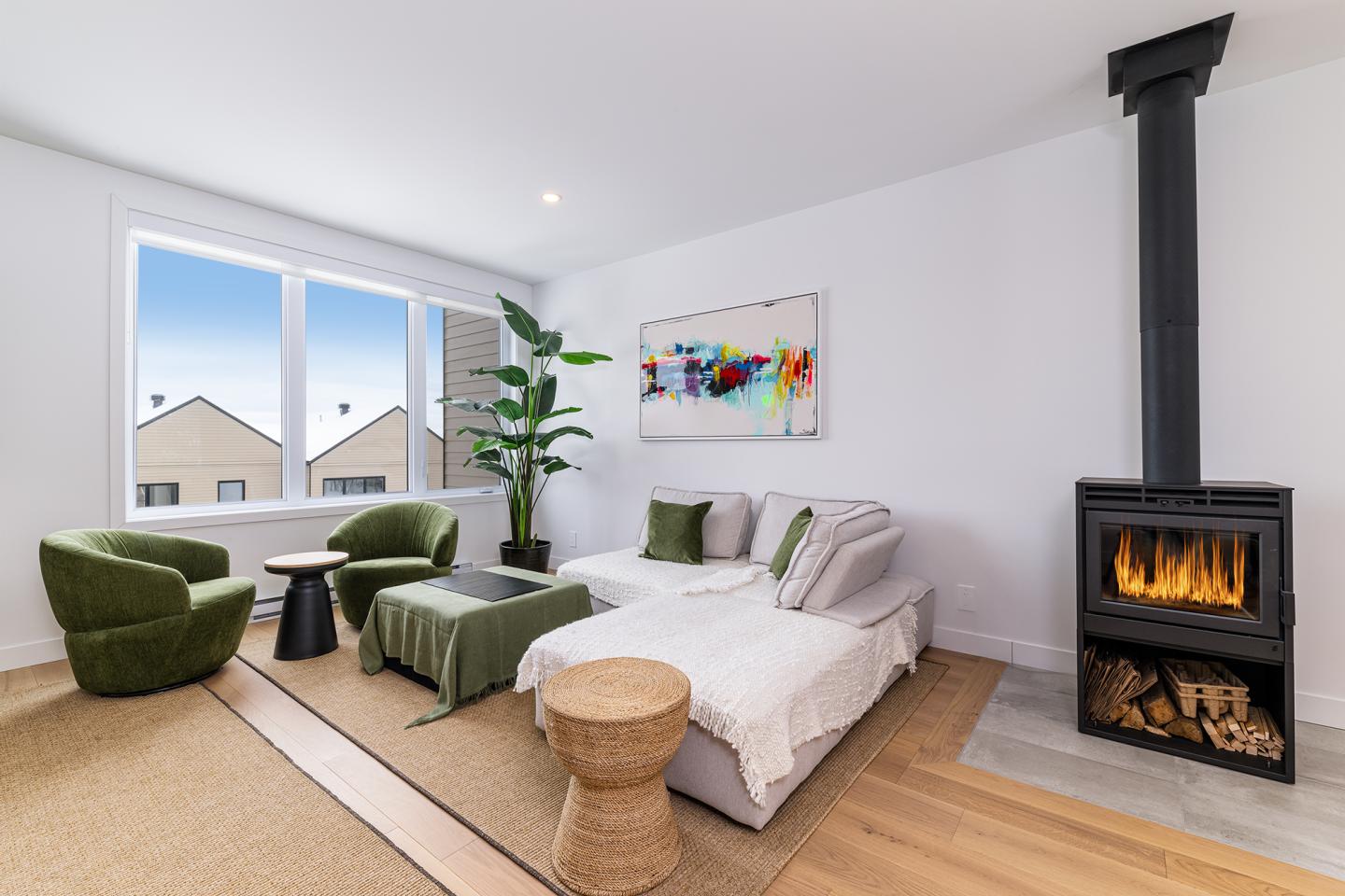 Salon moderne avec canapé, poêle à bois, deux fauteuils verts et décoration colorée.