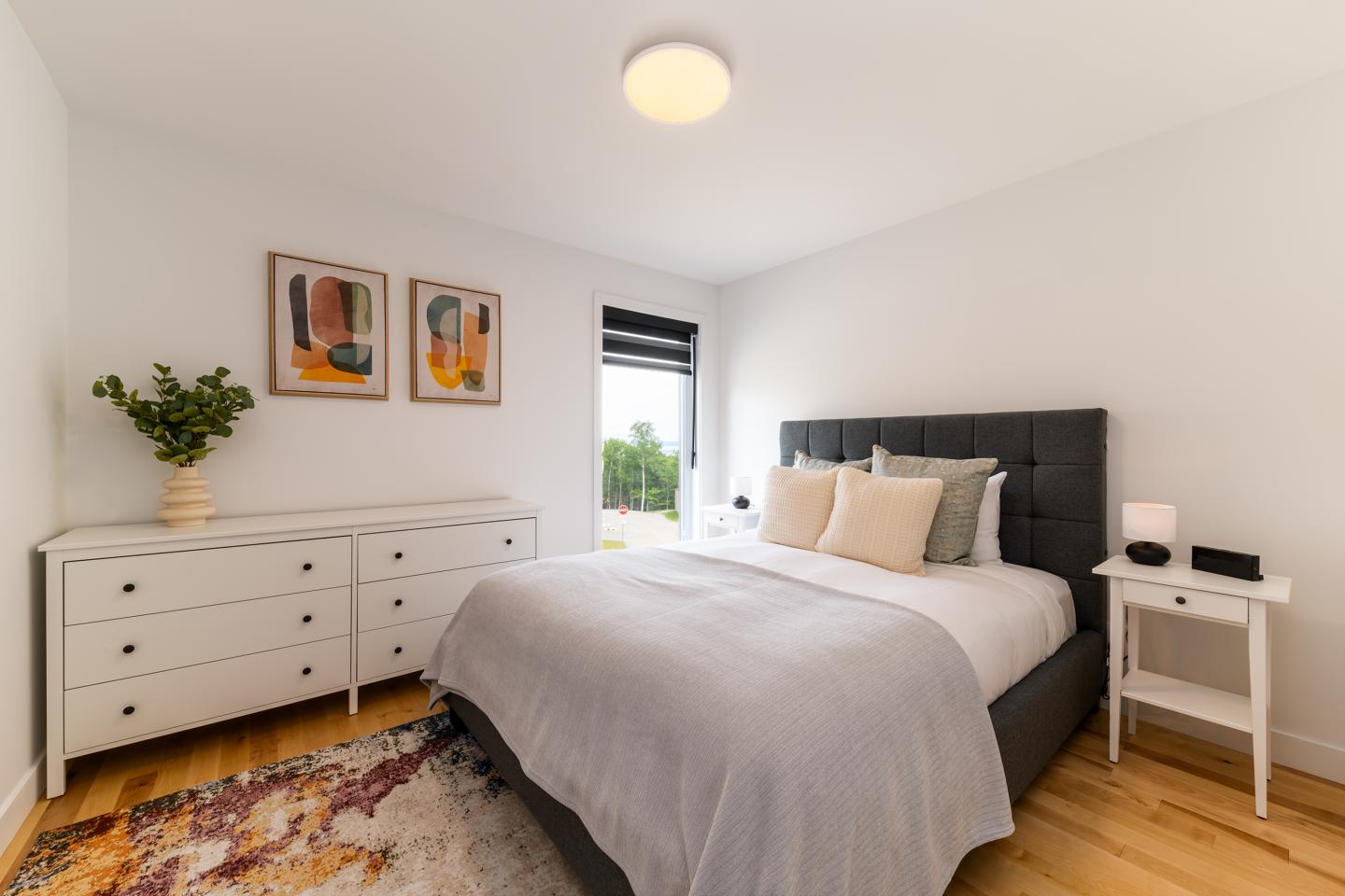 Chambre lumineuse avec lit double, commode blanche, et deux tableaux modernes.