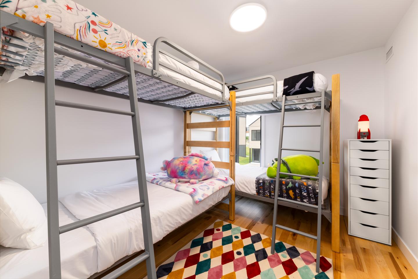 Chambre colorée avec deux lits superposés et un tapis à motifs géométriques.