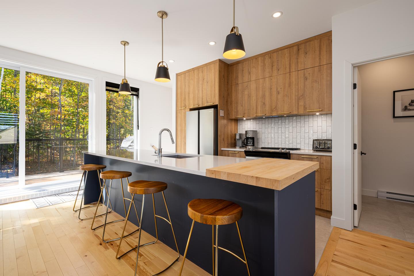Cuisine moderne avec îlot central, tabourets en bois, et luminaires pendants.
